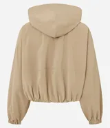 Campera cortavientos de color beige con diseño balonê, capucha con cordones ajustables, cierre frontal de cremallera y puños con elástico. Presenta un corte holgado y moderno.