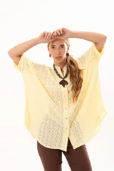 Camisa de corte oversize y mangas murciélago, confeccionada en tela con perforaciones tipo broderie. Presenta cuello mao, cierre frontal con botones y un diseño holgado y fluido.