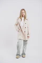 Trench color beige con doble botonadura, solapas amplias, cinturón en la cintura y presillas en los puños.