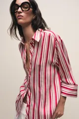 Camisa de cuello solapa con estampado de rayas verticales en tonos rojos, rosas y blancos. Presenta cierre frontal con botones y mangas por debajo del codo con terminación en vuelta.