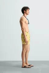 Bañador de hombre de tejido técnico ripstop, color mostaza con estampado floral abstracto en blanco y negro. Presenta cintura elástica ajustable con cordón, bolsillos laterales y bolsillo trasero de plastrón.