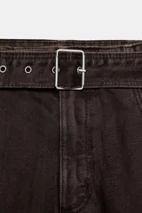 Pantalón cargo de tiro medio confeccionado en denim marrón oscuro. Presenta bolsillos laterales con solapa, bolsillos clásicos y un cinturón integrado del mismo tejido con hebilla metálica.