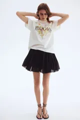 Remera de algodón color blanco crudo, corte oversized y cuello redondo. Presenta un estampado central de flores silvestres con la palabra "BLOOMS" en tipografía serif negra, y las palabras "FLORIST" y "HARVESTS" a los lados.