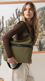 Cartera tipo hobo de tamaño grande en color beige, con detalles en negro. Presenta una franja horizontal negra con el logo de la marca, asa corta de hombro y correa larga desmontable. Incluye bolsillo frontal con cierre oculto y bolsillo trasero.