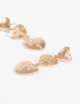 Par de caravanas colgantes doradas con forma de corazón. Un corazón pequeño liso en la parte superior y un corazón más grande con textura y strass en la parte inferior.