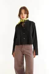 Blusa negra de manga larga con diseño de tablas verticales en el frente, cuello tipo mao y puños prolongados con abertura.