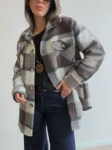 Sobrecamisa de paño con diseño a cuadros en tonos marrones, grises y blancos. Presenta cuello clásico, cierre frontal con botones y bolsillos delanteros con tapa.