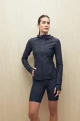 Campera deportiva negra de calce entallado, con cierre frontal completo, capucha integrada y mangas largas con puños envolventes. Presenta costuras estratégicas que estilizan la silueta y bolsillos laterales funcionales.