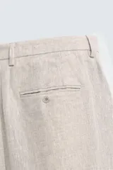 Pantalón de traje regular fit confeccionado en tejido de lino, con bolsillos laterales y bolsillos traseros de vivo con botón. Presenta cierre frontal con cremallera y botón.