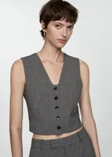 Chaleco de corte crop y diseño recto con cuello en pico y cierre frontal de botones. Presenta un estampado de raya diplomática y cuenta con forro interior y detalle de cinta en la parte posterior.
