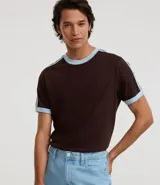 Remera de manga corta color marrón oscuro con cuello redondo y ribetes en contraste celeste claro en el cuello y los bordes de las mangas. Presenta dos finas rayas celestes a lo largo de los hombros.