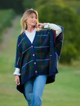 Poncho tejido de lana con diseño de cuadros en tonos azul, verde y rojo. Presenta escote en V, cierre frontal con botones de madera y bordes acanalados en color azul marino.