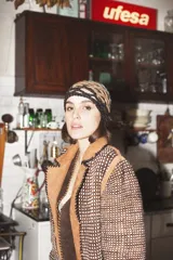 Tapado artesanal de lana con diseño de tejido de red en tonos marrones y negros. Presenta apliques de cuero natural en los bordes y una terminación de flecos largos en el ruedo.