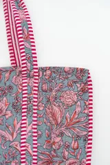 Bolso tipo tote bag de tela acolchada con estampado floral en tonos gris y blanco. Presenta asas largas reforzadas con detalle de rayas en los bordes.