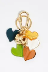Llavero de metal dorado con mosquetón y argolla, decorado con múltiples dijes de corazones de resina en colores verde, naranja, amarillo, blanco y azul oscuro, y cuenta con un abalorio central esférico dorado con el logotipo de la marca grabado.