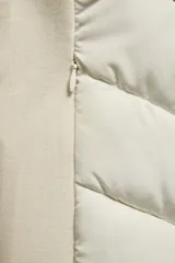 Cazadora de mujer con diseño híbrido, presenta un panel frontal acolchado con costuras en chevron y mangas y laterales en tejido liso. Cuenta con cuello alto, capucha ajustable con cordones elásticos y cierre frontal mediante cremallera.