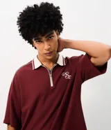 Remera de punto color bordó con ribetes blancos en los hombros y cuello polo, de corte holgado y manga corta. Cuenta con un diseño estampado en la espalda con texto en tonos claros.