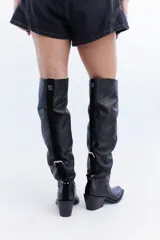 Bota de cuero negro de caña alta slouchy, con diseño fruncido ajustable mediante un juego de correas y hebillas. Presenta taco bajo cuadrado y punta cuadrada.