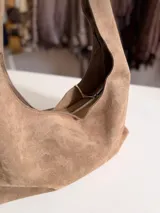Cartera tipo hobo de diseño flexible y caída natural, confeccionada en material con textura simil gamuza. Cuenta con asa corta integrada para llevar al hombro, cierre superior y bolsillo interior con cierre.