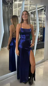 Vestido largo azul metálico con escote cuadrado, tirantes finos y espalda con tiras cruzadas. Presenta una abertura lateral en la falda.