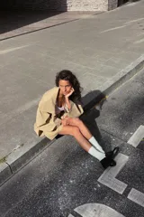 Trench color beige con cuello de solapa subido y manga larga. Tiene bolsillos laterales, forro interior y cinturón de lazo en el mismo tejido. El cuello se cierra con un botón.