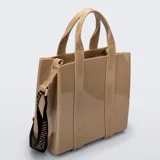 Cartera tipo tote bag Melissa modelo Dulce Bag, color tostado, fabricada en plástico PVC brillante. Cuenta con asas de mano fijas, tiras decorativas verticales con el logotipo de la marca y una correa larga ajustable y desmontable en color negro con inscripciones.