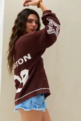 Sweater de punto marrón chocolate, con diseño oversize, cuello en V, mangas largas con estrellas blancas estampadas y número grande en el frente.