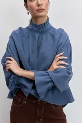 Camisa azul de manga larga con cuello alto fruncido y puños elásticos.