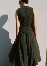 Vestido midi evasé color verde oscuro, sin mangas con tirantes anchos, cuello redondo y detalle de pañuelo cruzado en la cintura con lazo lateral. Cuenta con cierre de cremallera lateral.