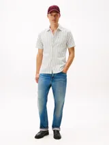 Camisa de manga corta de algodón, color blanco con rayas verticales finas en verde. Presenta cuello clásico con abertura en V y un bolsillo de parche en el pecho con logo bordado.