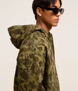 Campera con capucha y cierre frontal, confeccionada en sarga con estampado camuflado. Tiene manga larga con sisa desplazada, puños ajustados, bolsillo canguro y bajo con elástico.