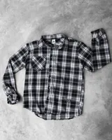 Sobrecamisa de franela a cuadros blancos, negros y grises, de manga larga, con cuello camisero, cierre abotonado y bolsillo en el pecho.