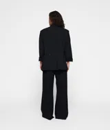 Blazer oversize negro confeccionado en crepé con forro de algodón y viscosa. Presenta hombreras, cuello con solapa y cierre de botón, dos bolsillos de solapa, bordado a mano en la espalda, un falso bolsillo de ribete en la espalda y dos aberturas en la espalda.