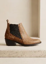Bota tipo Chelsea de cuero, con paneles laterales elásticos en color negro y talón en gamuza. Presenta un taco bajo cuadrado y una lengüeta en la parte superior trasera.