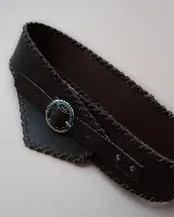 Faja de cuero negro con diseño ancho y costuras decorativas en los bordes. Presenta una hebilla metálica circular plateada en el centro y un diseño asimétrico en la parte frontal.