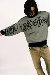Sweater reversible de tejido de punto con diseño gráfico estilo tribal. Un lado presenta base negra con detalles en gris, mientras que el otro lado presenta base gris con detalles en negro. Posee cuello redondo, mangas largas y puños acanalados.