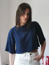 Top corto azul marino de punto, con mangas cortas amplias, cuello redondo y detalle de escudo bordado en la parte delantera.