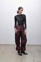 Pantalón de tafeta tornasolada color borgoña, de corte recto y tiro alto, con cintura elastizada, bolsillos frontales con cierre y cordones ajustables en las pantorrillas para fruncir el bajo.