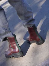 Botas de cuero marrón con suela track de goma negra, cierre lateral en color rojo y detalle de tira trasera al tono.