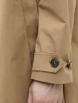 Campera tipo trench coat de corte recto y largo medio, color tostado. Presenta cuello camisero, cierre frontal con botones oscuros y puños ajustables con trabilla y botón.