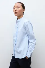 Camisa de manga larga a rayas celestes y blancas, con cuello mao y volados verticales en el frente.