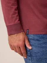 Remera de manga larga con cuello redondo y cierre frontal parcial con botones. Presenta un diseño de color sólido con un pequeño logo bordado en el pecho.