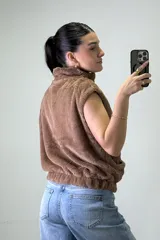 Chaleco de piel sintética color beige, con cuello alto, cierre frontal y bolsillos laterales.