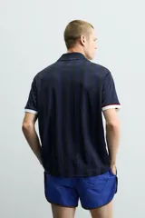 Polo de corte relajado confeccionado en tejido técnico, con diseño de rayas verticales en tonos azul marino y negro. Presenta cuello solapa con abertura frontal y detalles de rib en contraste en cuello y mangas. Incluye estampado frontal con el número 98 y la inscripción France, además de una etiqueta aplicada en el ruedo inferior.
