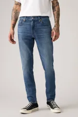 Pantalón de jean corte slim taper, con diseño de cinco bolsillos, cierre de cremallera y botón metálico, en tono azul medio con efecto lavado.