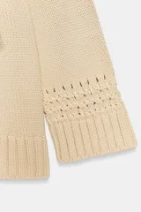 Chaqueta cruzada de punto color beige con manga larga, cuello smoking y cierre frontal con lazada. Presenta detalles de calados en los puños.
