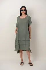 Vestido midi de lino color beige, de corte holgado y silueta acampanada. Cuenta con cuello redondo, mangas cortas amplias, bolsillos laterales y detalles de recortes horizontales en la falda con terminación asimétrica más larga en la parte trasera.