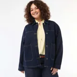 Chaqueta vaquera de corte largo y holgado, color azul oscuro con costuras en contraste. Presenta cuello clásico, cierre frontal con botones metálicos y dos grandes bolsillos frontales de parche.