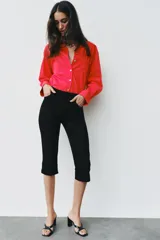 Camisa de popelina roja, de corte oversize, con cuello solapa, manga larga y bajo asimétrico redondeado. Cierre frontal oculto con botones.