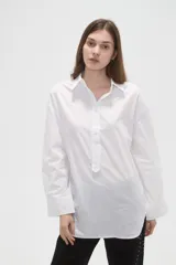 Camisa de algodón blanca de corte holgado, con cuello clásico, cierre frontal parcial con botones y mangas largas con puños anchos.